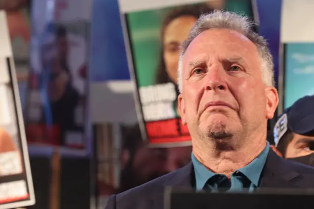 Witkoff regarde droit devant lui, le visage grave, tandis que des pancartes sont brandies derrière lui montrant les visages d'otages israéliens détenus à l'époque par le Hamas à Gaza.