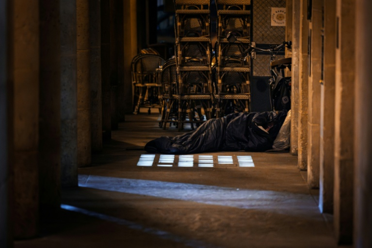 Un homme dort dans un sac de couchage à proximité d'une terrasse de café le 15 octobre 2025 à Paris ( AFP / JOEL SAGET )