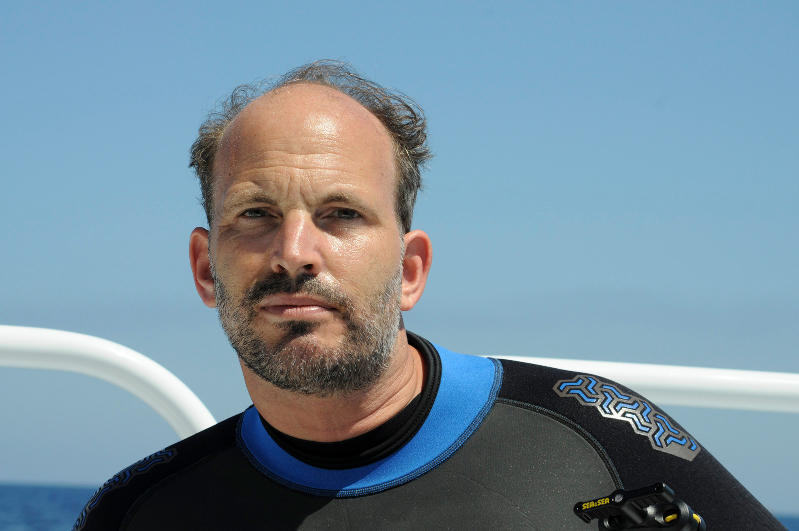 Un homme barbu en combinaison de plongée avec une mer bleue en arrière-plan. Un homme barbu en combinaison de plongée avec une mer bleue en arrière-plan.