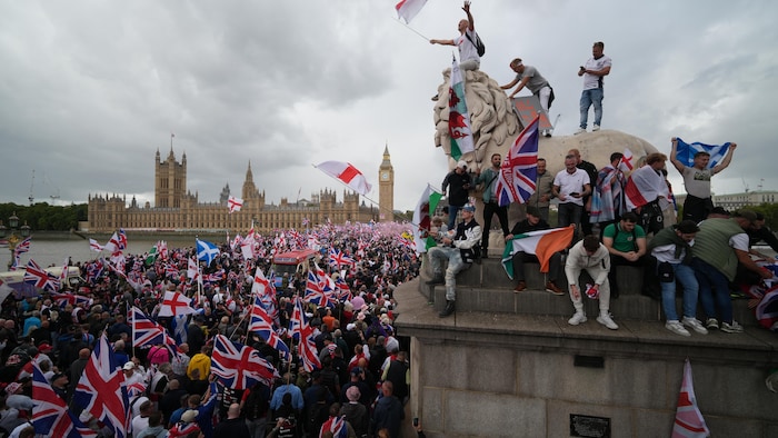 Des manifestants brandissent des drapeaux et grimpent sur une statue près de la Tamise, à Londres.