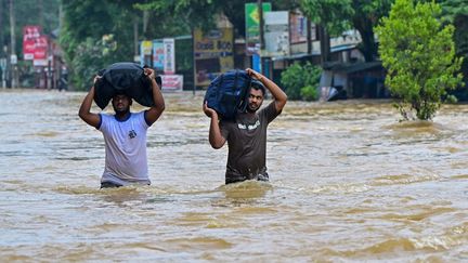 Des habitants portent leurs affaires sur une route inondée après des pluies diluviennes à Kaduwela, en périphérie de Colombo (Sri Lanka), le 29 novembre 2025. (ISHARA S. KODIKARA / AFP)