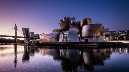 En 1997, l'inauguration du musée Guggenheim de Bilbao, en Espagne, assoit la réputation internationale de l'architecte et demeure l'un des projets les plus emblématiques. Le bâtiment, fait de roche calcaire, de verre et de courbes en titane, reflète la lumière et l'avant-gardisme de Frank Gehry. (FRANCOIS LAURENS / HANS LUCAS / AFP)