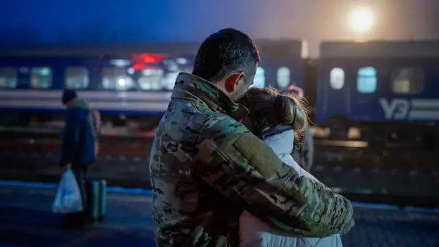 Un homme en uniforme militaire serre une fille dans ses bras avant le départ du train