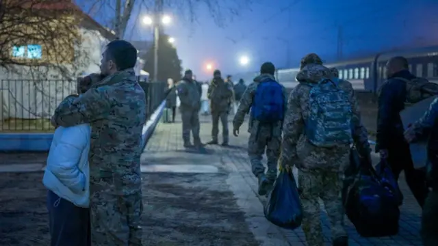 Un couple s'embrasse sur le quai de la gare tandis que des soldats passent.