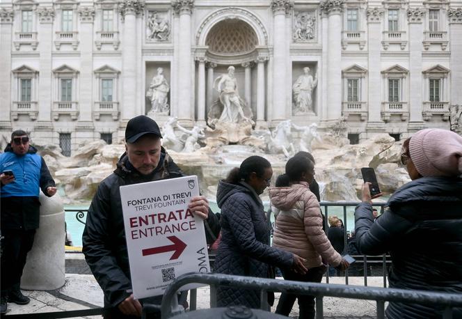 Un homme tient une pancarte sur laquelle est inscrit « Entrée » devant la fontaine de Trevi, à Rome, le 19 décembre 2025.