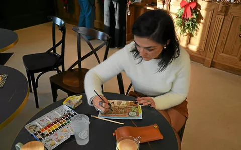 Sur sa table, une palette bien creusée, des pinceaux en bois et un carnet bien rempli.