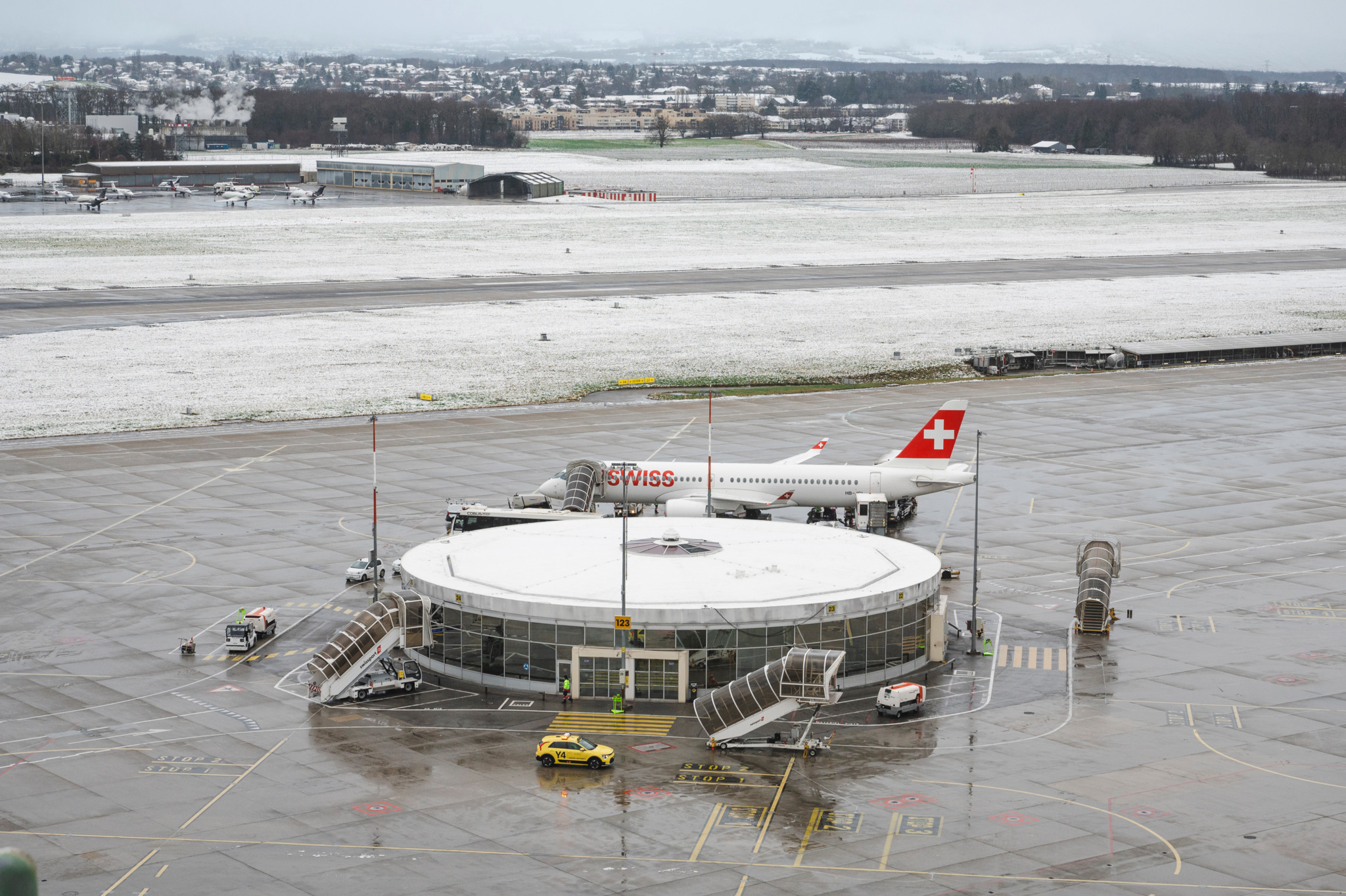 Vue aérienne de l’aéroport de Genève avec un avion de la compagnie Swiss stationné en piste. Neige légère sur les environs.
