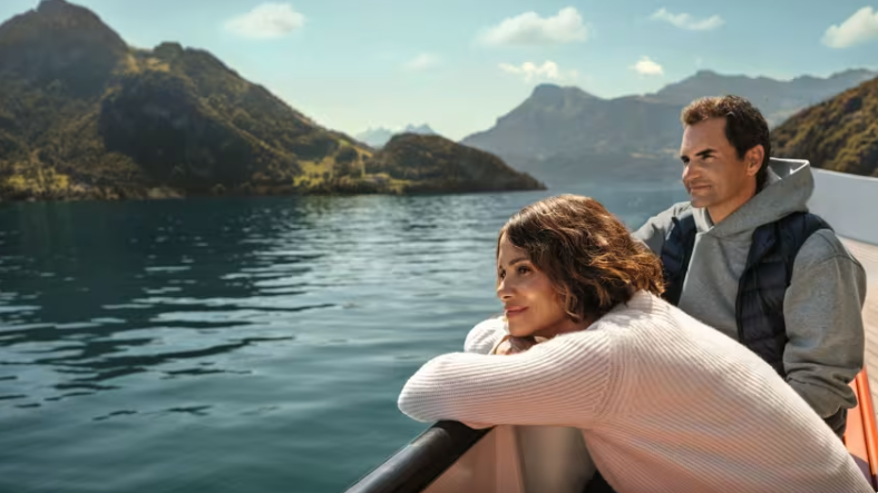 Deux personnes profitant d’une vue panoramique sur un lac entouré de montagnes sous un ciel bleu.