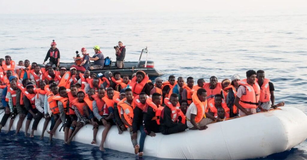 Migrants portant des gilets de sauvetage entassés sur un canot pneumatique en Méditerranée, secourus par une équipe humanitaire en mer.