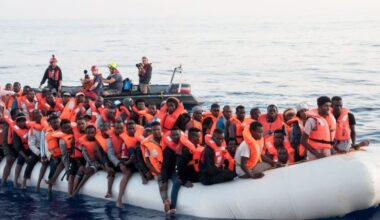 Migrants portant des gilets de sauvetage entassés sur un canot pneumatique en Méditerranée, secourus par une équipe humanitaire en mer.