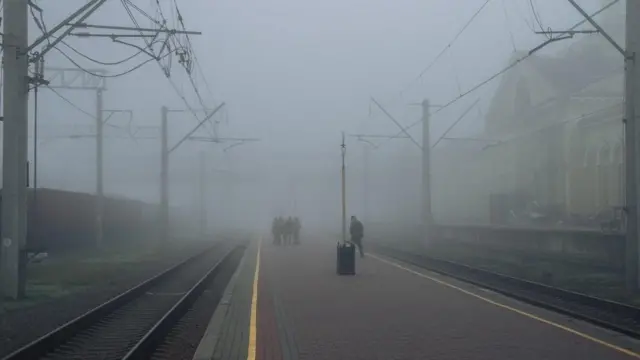 Une gare ferroviaire dans le brouillard et des personnes en uniforme militaire.