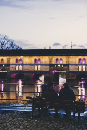 Couple de dos sur un banc devant le barrage Vauban éclairé de rose –