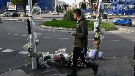 Un piéton passe devant les bouquets de fleurs déposés à l'endroit où Mehdi Kessaci a été assassiné, à Marseille, le 18 novembre 2025. (CHRISTOPHE SIMON / AFP)
