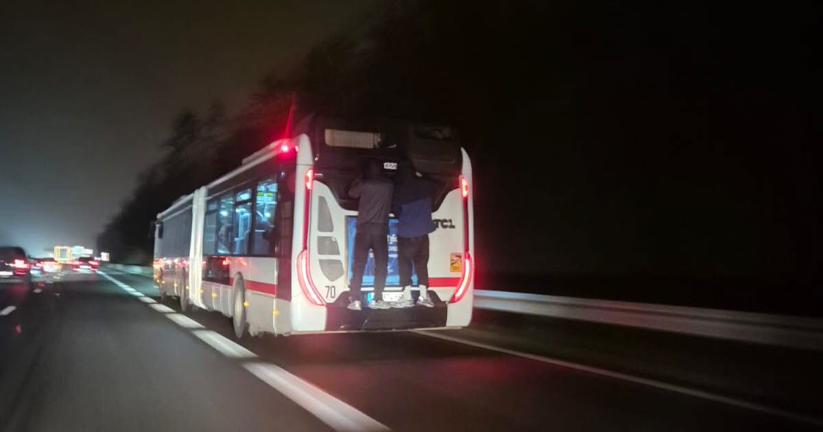 deux personnes filmées accrochées à l’arrière d’un bus qui roule sur la M6