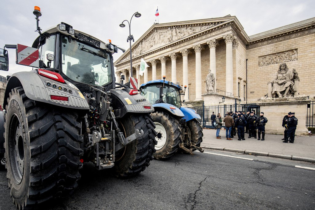 Photo montrant deux tracteurs stationnés devant l'Assemblée nationale à Paris. On peut voir des forces de l'ordre à côté.