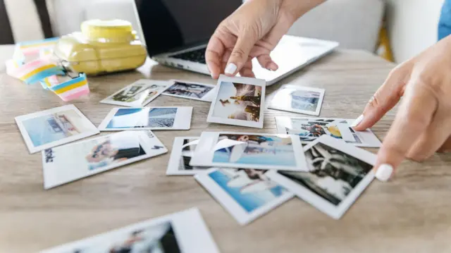 Une personne avec les ongles peints en blanc regarde des photos imprimées sur une table