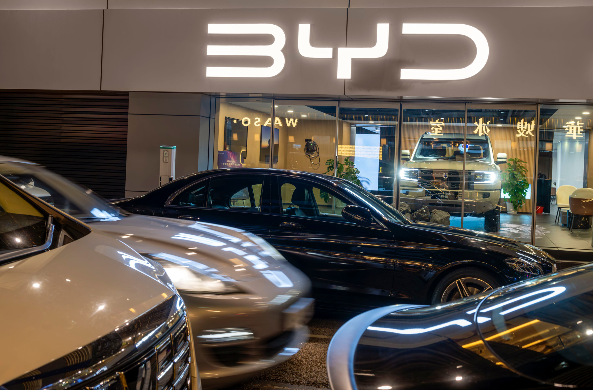 Vitrine du showroom de voitures BYD à Hong Kong avec plusieurs véhicules garés devant sous le logo lumineux BYD.