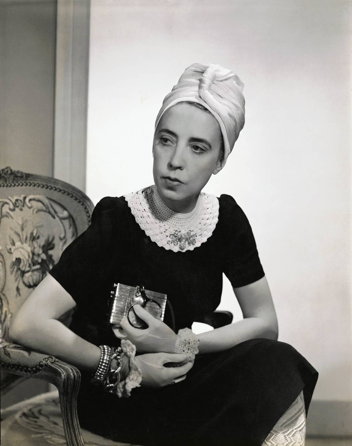 Designer Elsa Schiaparelli wearing black silk dress with crocheted collar of her own design and a tuban.