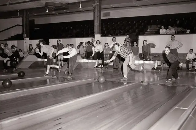 Image en noir et blanc de jeunes gens jouant au bowling.