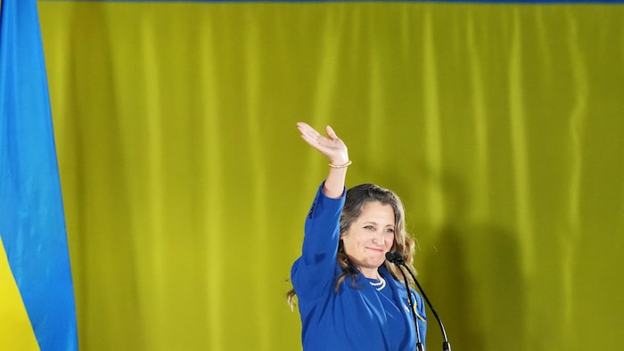 Chrystia Freeland salue la foule devant un drapeau ukrainien.