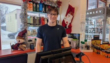 Le jeune homme sourit derrière la caisse d'un magasin.