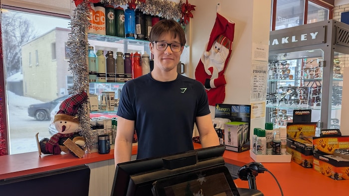 Le jeune homme sourit derrière la caisse d'un magasin.