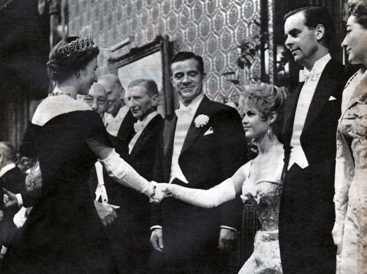 La jeune Brigitte Bardot fait la révérence et salue la reine Elizabeth II, entournée notamment par les acteurs Dana Andrews (à la droite de la jeune femme) et Joan Crawford (à droite sur la photo), le 29 octobre 1956, à Londres. (CCI / SHUTTERSTOCK / SIPA)