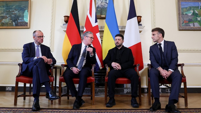 Friedrich Merz, Keir Starmer, Volodymyr Zelensky et Emmanuel Macron sont assis côte à côte devant leurs drapeaux respectifs dans une salle.
