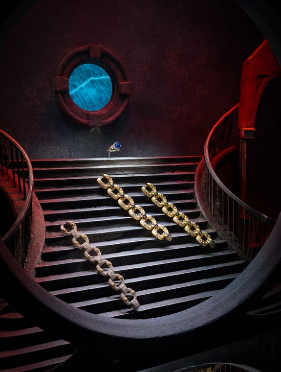 Elegant jewelry pieces arranged on a spiral staircase with a circular window in a dimly lit, atmospheric setting.