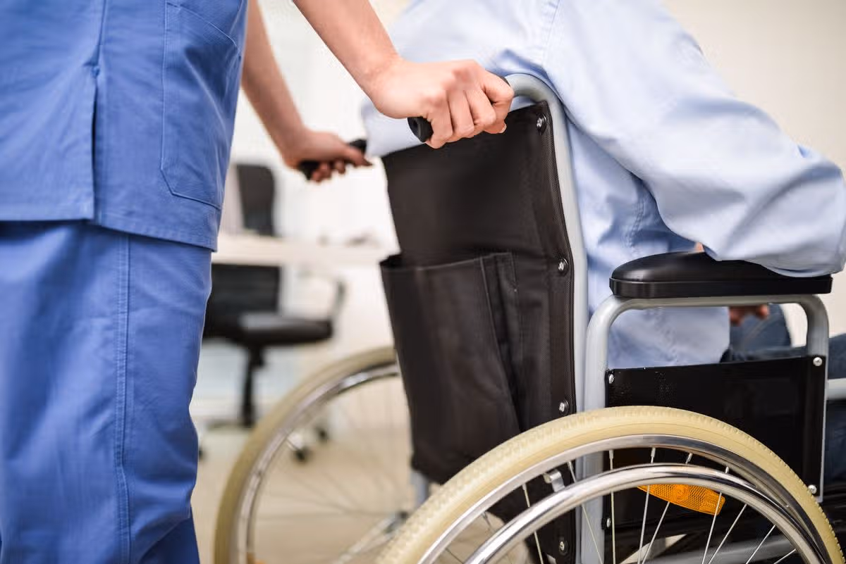 A nurse pushes a disabled man in a wheelchair [stock image]