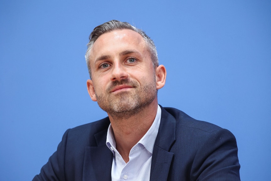 Ulrich Siegmund looks happy against a blue background.