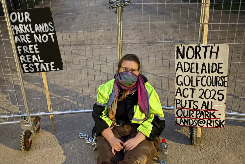 A protester sits by a gate of the North Adelaide Golf Course redevelopment.