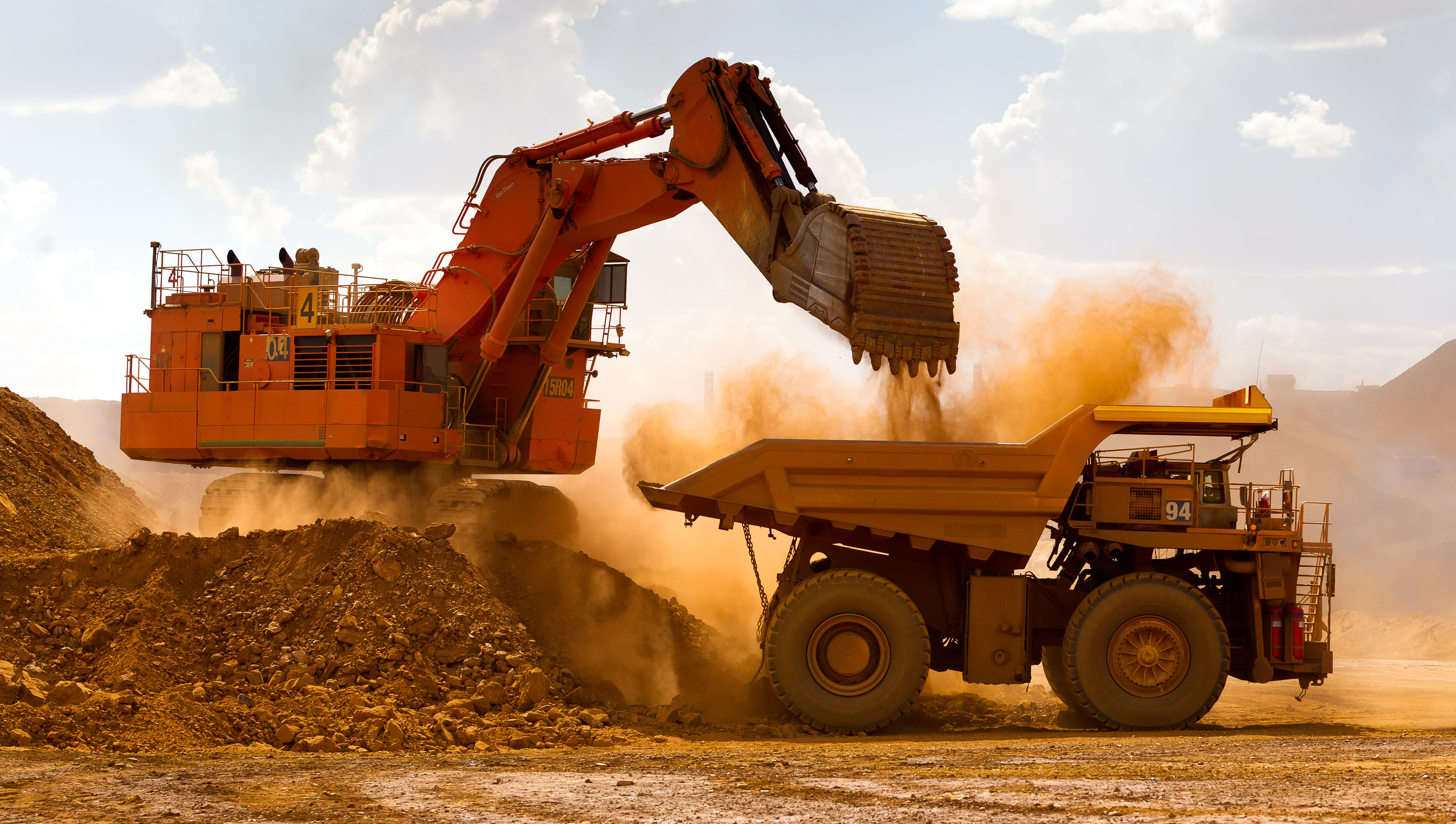 A large excavator loading ore into a haul truck at a mine.