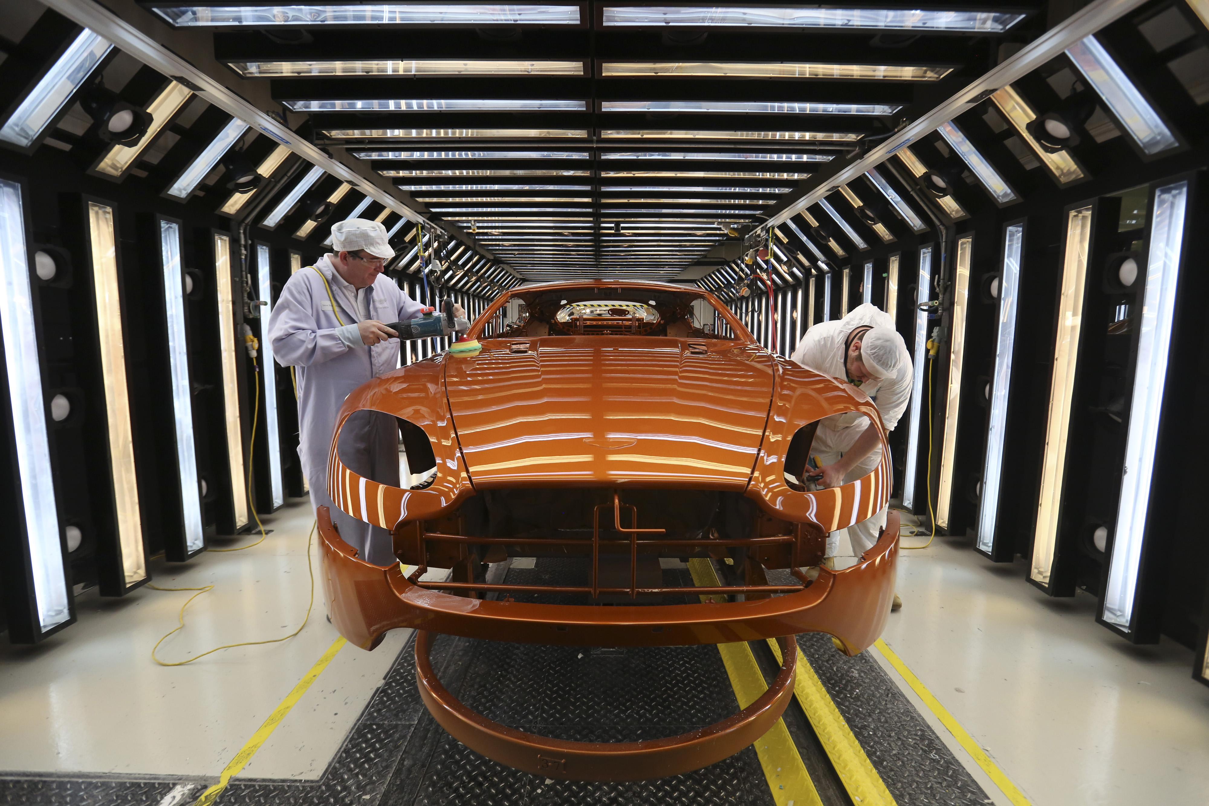 Workers polishing an Aston Martin V8 Vantage in a paint shop.