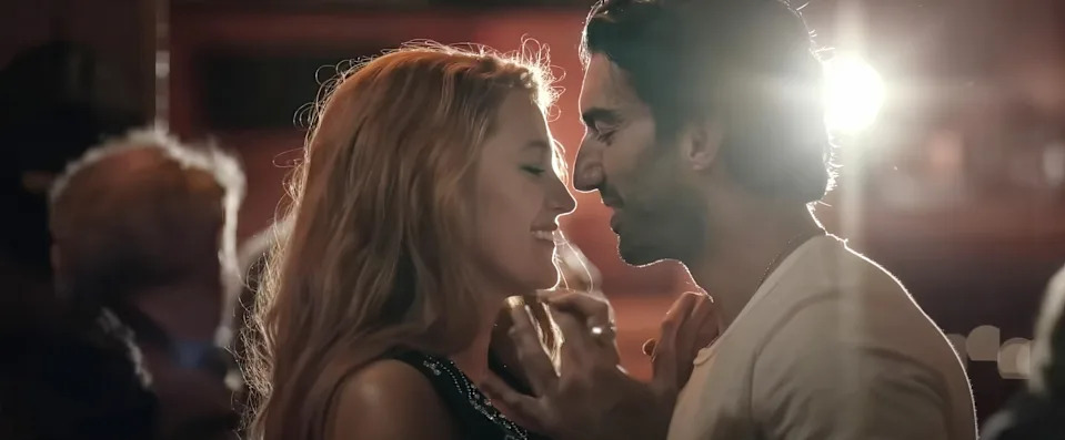 A couple sharing an intimate moment, standing close and smiling at each other in a softly lit setting