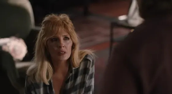 A woman with long hair, wearing a checkered shirt, looks upwards with a concerned expression