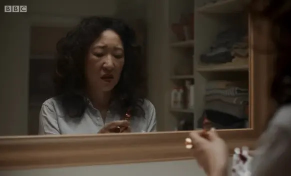 A person looks worried while holding an object, standing in front of a bathroom mirror