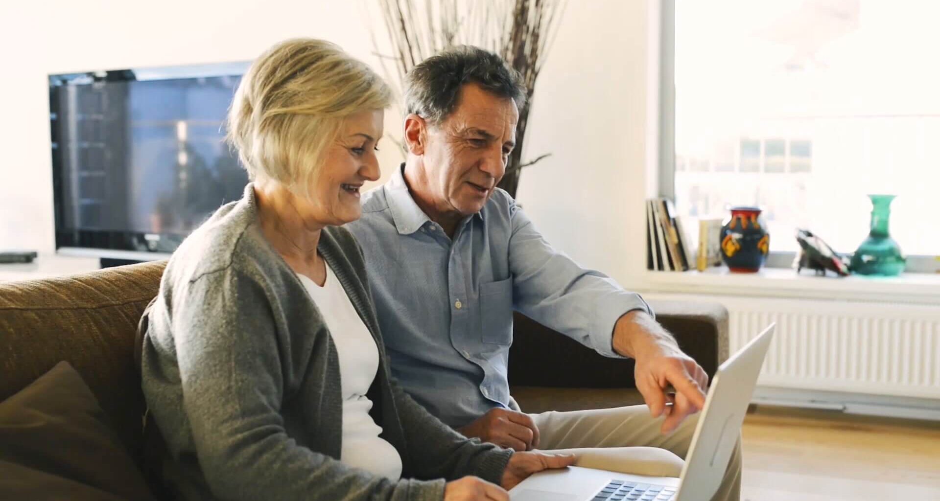 A couple sitting on a couch looking over financials on a laptop.