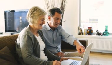 A couple sitting on a couch looking over financials on a laptop.