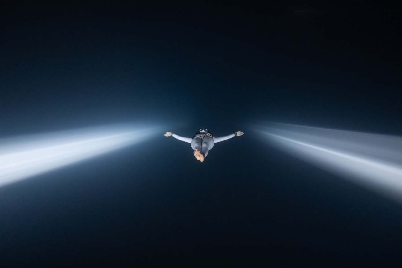 Freediver Surya Lecona Moctezuma diving down in between light beams