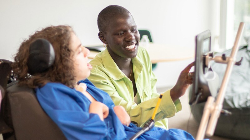A person using an assistive device for another person in a wheelchair.