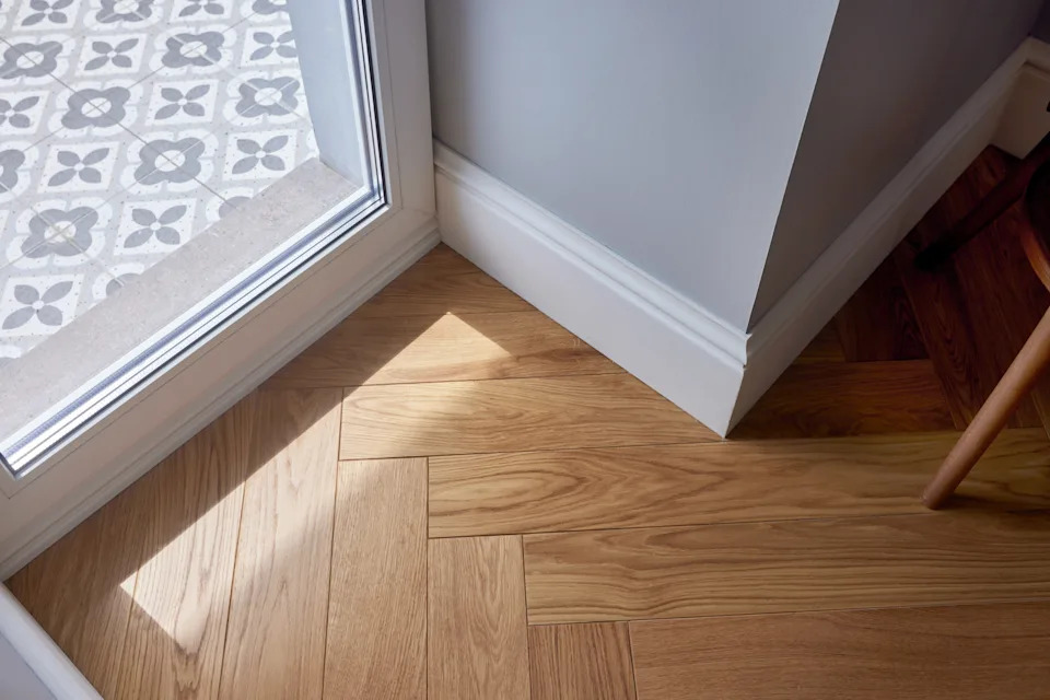 The sunlight filters through the glass door, illuminating a cozy nook with a wooden floor and stylish tiled entryway. This contemporary design exudes warmth and invites a welcoming atmosphere into the space