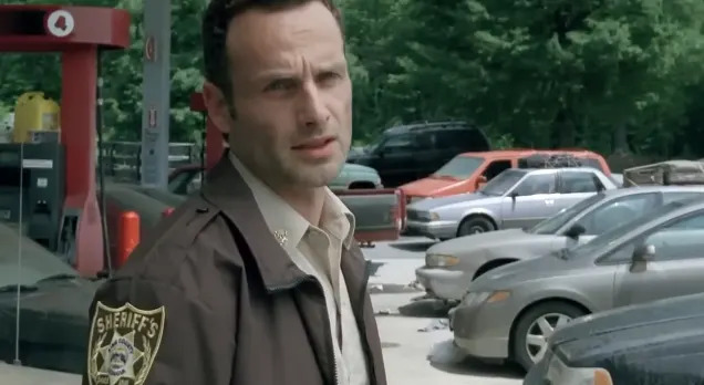 Man in sheriff uniform standing by parked cars at a gas station