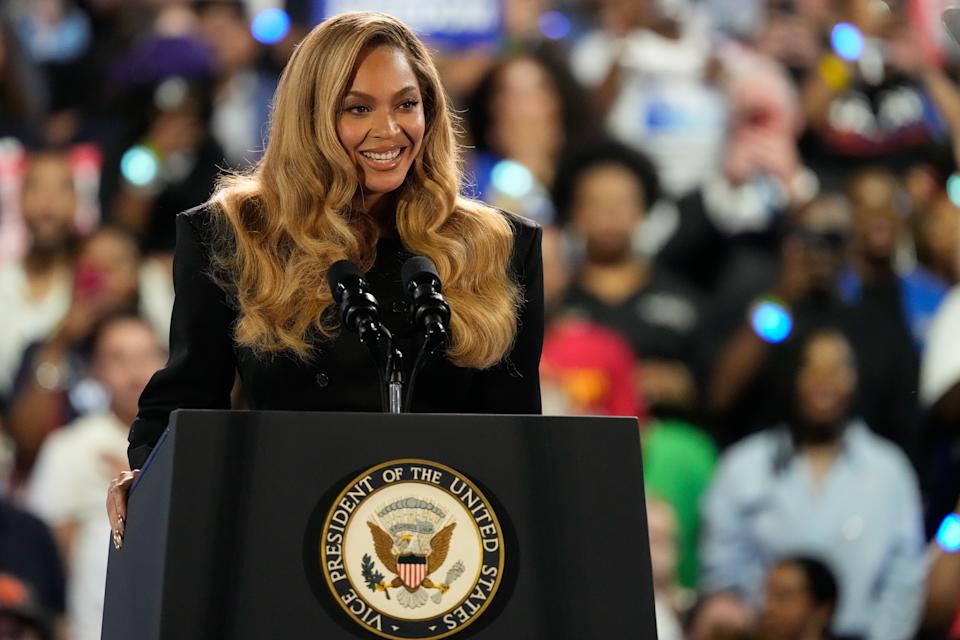 Beyonce with wavy hair stands confidently at a podium with the U.S. presidential seal, speaking to a crowd