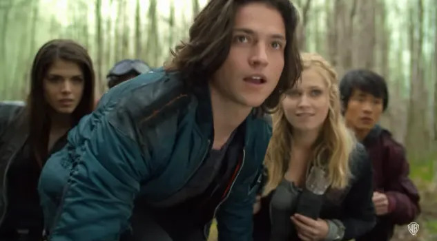 A group of young adults looks intently forward in a forest scene, appearing focused and ready for action