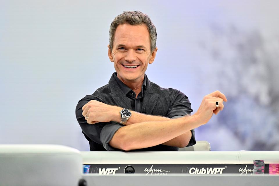 Neil Patrick Harris smiling, sitting at a poker table during an event