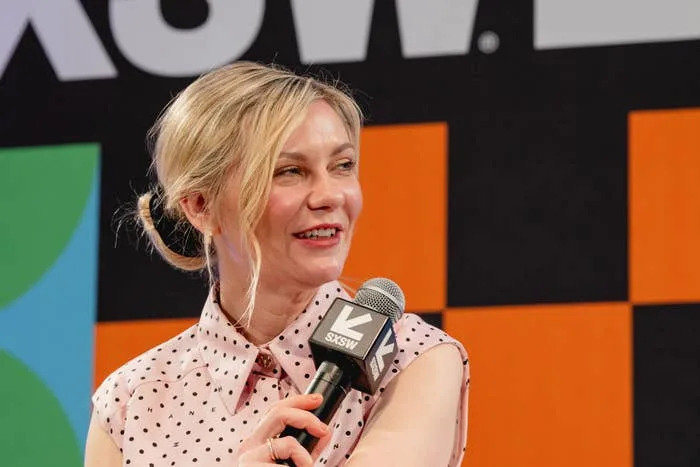 Kirsten Dunst in a polka dot top speaks into a microphone at a SXSW event