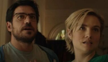 Diego and Sage, a Brazilian man and a white woman, stand in a dimly lit mansion while looking at something out of frame in shock in a still from the horror movie Bone Lake.