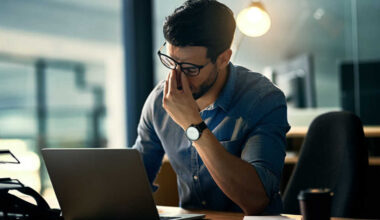 A person working on the computer, rubbing their eyes as if they are tired.