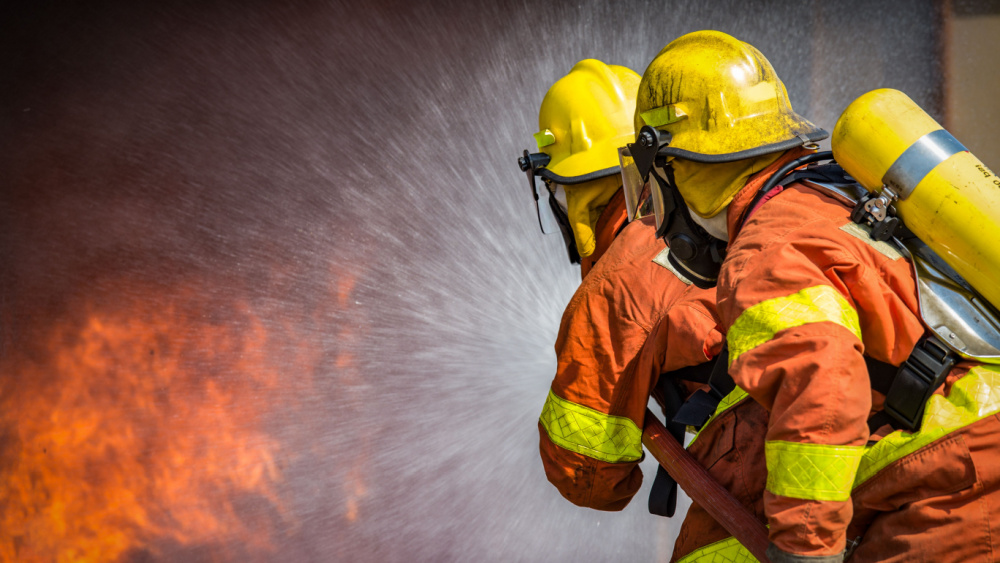 2 firefighters in full gear fighting a fire.